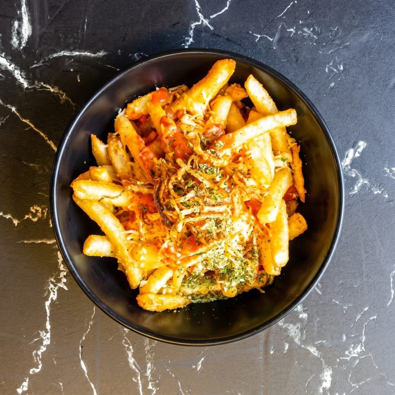A black bowl filled with golden french fries, drizzled with sauce, cheese, and herbs.