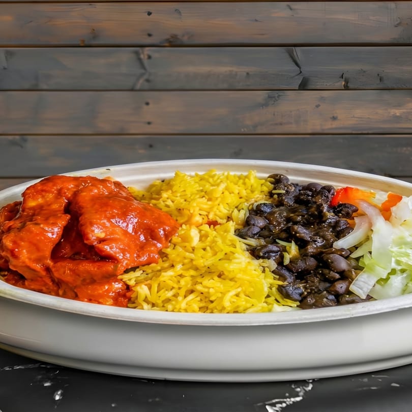 A colorful bowl with red chicken, yellow rice, black beans, and fresh lettuce.